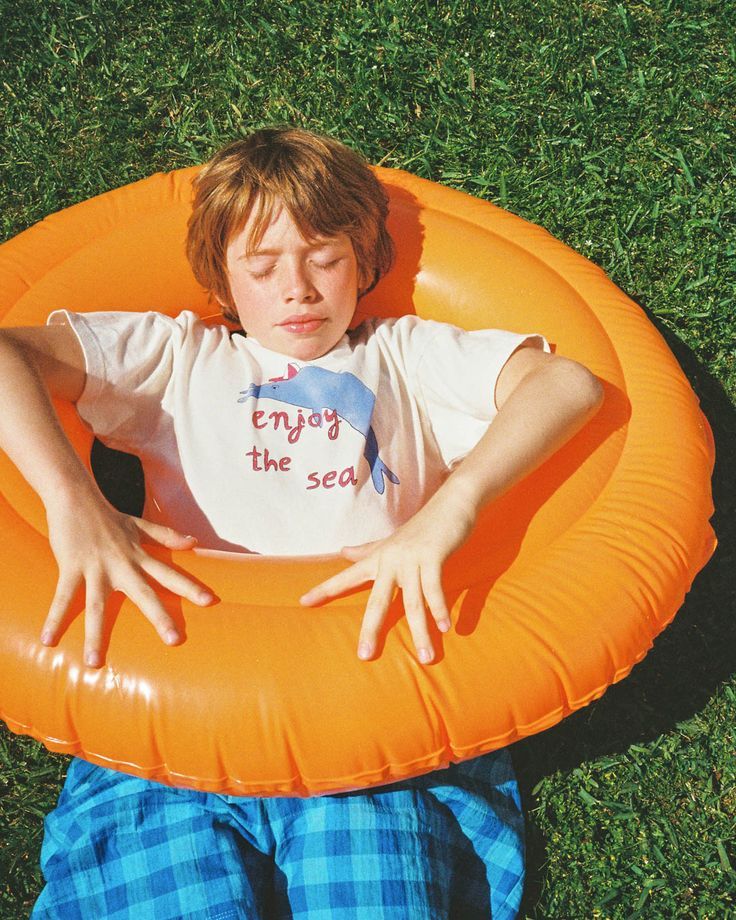 A boy lying back in an orange swim ring on the grass