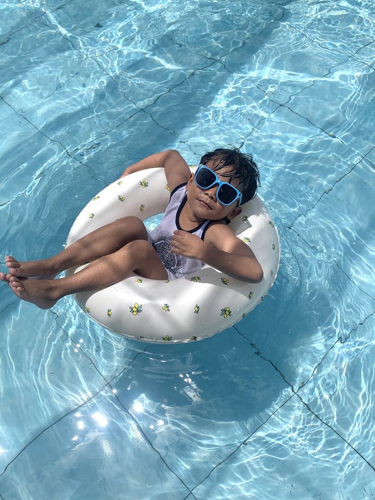 A boy in blue sunglasses relaxing in a swim ring in the pool