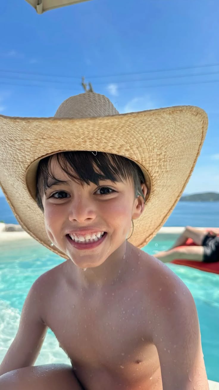 A grinning boy in a big straw hat beside a pool