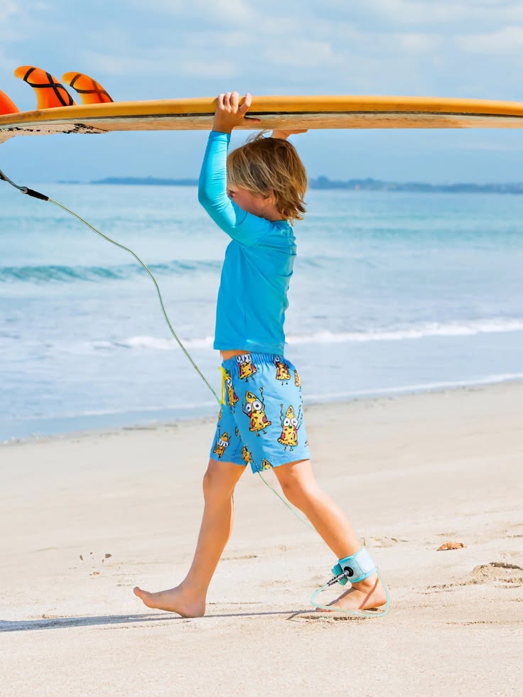 A boy carrying a surfboard over his head along the beach