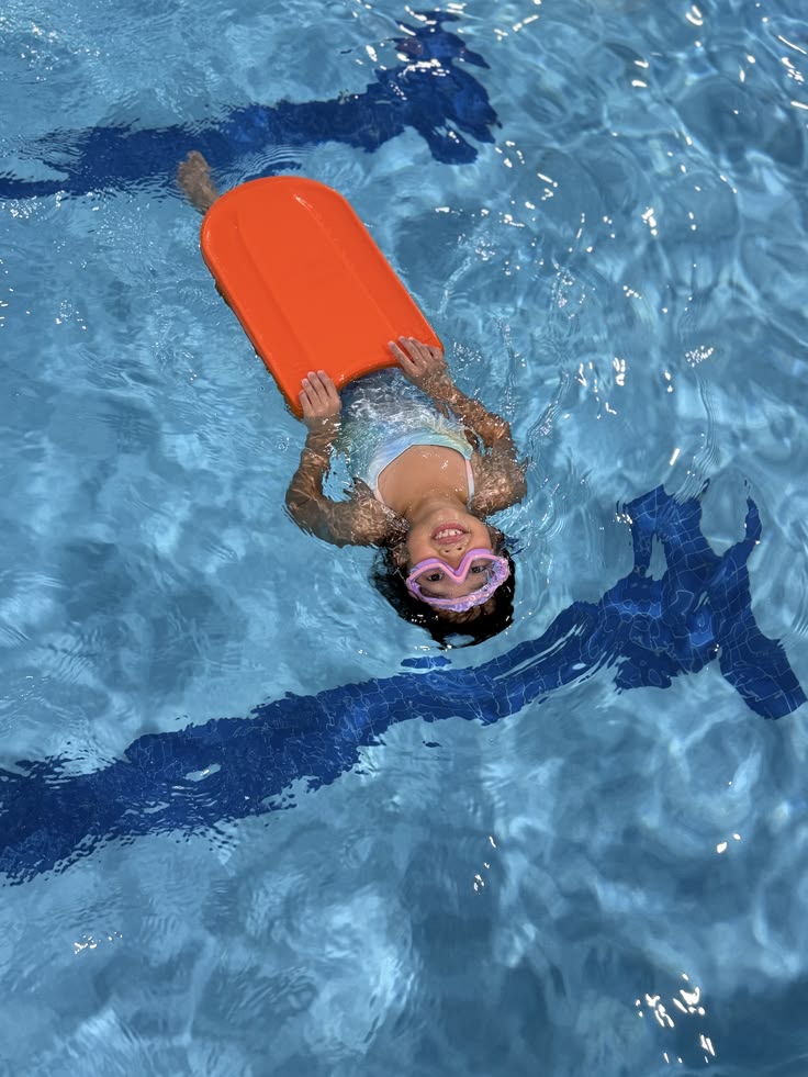 A girl floating on her back in the pool, holding an orange kickboard